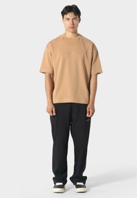 Béžové bavlněné tričko s kulatým výstřihem a krátkým rukávem, kombinované s černými kalhotami s jemným brandingem a volným střihem.