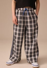 Pantalons de pyjama à carreaux noirs et blancs avec une coupe loose, ceinture élastique et cordon de serrage bleu, comportant des rayures sur les côtés et des poches.