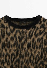 Pull à imprimé léopard en tissu doux et duveteux. Base beige terre avec des taches noires. Présente un col rond noir et une étiquette à l'intérieur.