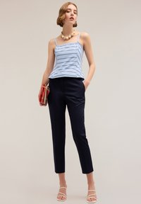Lichtblauwe gestreepte top met spaghettibandjes, gecombineerd met op maat gemaakte marineblauwe broek. Model houdt een rode clutch vast en draagt sandaaltjes met bandjes.