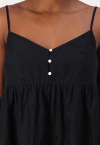 Svart sommerkjole med tynne stropper, v-hals, dekorative knapper og broderte blomsterdetaljer på myk stoff. Utsvingt skjørtedesign.