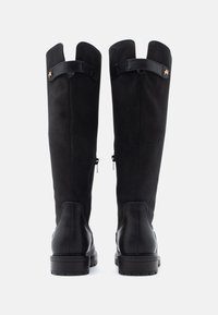 Botas altas negras de ante con una base de cuero suave. Cuentan con cierre de cremallera, punta redondeada y una correa decorativa en la parte superior.