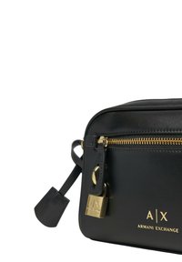 Borsa a tracolla sintetica nera con hardware dorato, chiusura con zip e dettaglio con lucchetto. Presenta un logo impresso sulla parte anteriore e un design elegante.