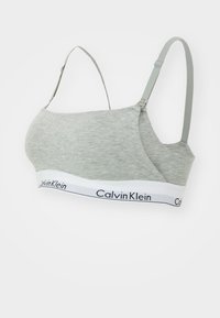 Calvin Klein pelēkā kokvilnas bralette ar regulējamām siksnām un baltu joslu ar melnu logos teksta. Gluda tekstūra un bezšuvju dizains.