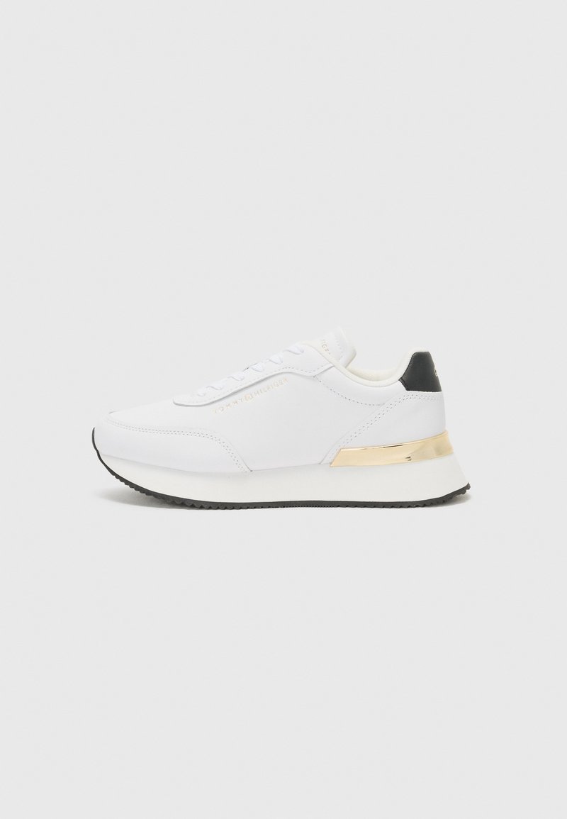 Sneaker bianco con finitura liscia, caratterizzato da un accento sul tallone nero e un dettaglio metallico dorato sulla suola intermedia. Design con lacci, suola in gomma.