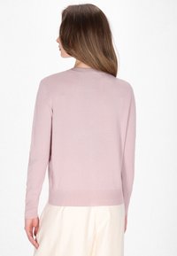 Pulover tricotat de culoare roz deschis, cu mâneci lungi, guler rotund și tiv zimțat. Textură fină, se potrivește strâns pe corp, cu detalii de design minime.