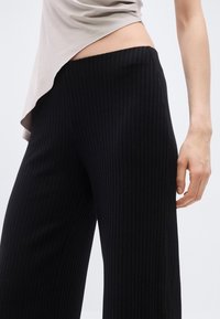 Μαύροι ριμπ ζιπ-κιλότ παντελόνες με υφή και ελαστική μέση, συνδυασμένοι με ανοιχτόχρωμο τοπ με καμπυλωτό τελείωμα.