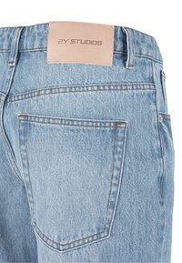 Jean en denim bleu clair avec une finition lisse, doté d'une étiquette en cuir sur la ceinture et d'une poche arrière avec des détails de couture subtils.