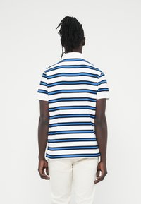 Πόλο με κοντό μανίκι σε λευκό χρώμα με οριζόντιες ρίγες σε μπλε και μαύρο, διαθέτει κλασικό γιακά και άνετη εφαρμογή.