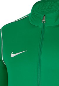 Grüne Sportjacke mit hohem Kragen und Reißverschluss vorne. Mit weißen Akzenten und Nike-Logo. Hergestellt aus glattem, atmungsaktivem Stoff.