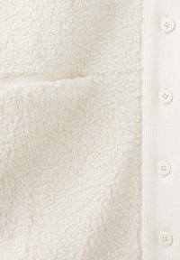 Gros plan sur un tissu sherpa polaire crème à côté d'un tissu côtelé avec des boutons crème assortis sur le côté droit.