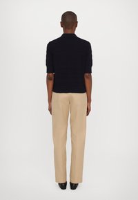 Polo a maniche corte blu navy in maglia con motivo strutturato, abbinata a pantaloni sartoriali beige. Vestibilità slim, tessuto liscio e design minimalista.