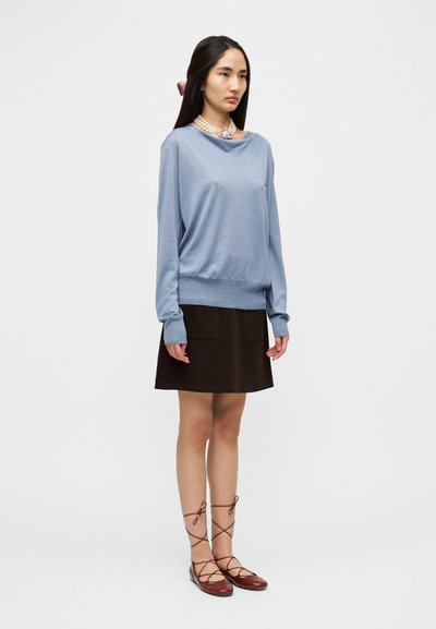 Ανοιχτό μπλε πουλόβερ με μακριά μανίκια και ριμπ τελείωμα, σε συνδυασμό με καφέ φούστα A-line με δύο μπροστινές τσέπες. Καφέ μπαλαρίνες με κορδόνια.
