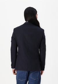 Navy blazer with a tailored fit, single back vent, and structured shoulders, paired with blue denim jeans. Smooth fabric texture.