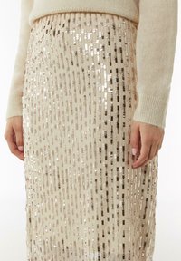 Cremefarbene Paillettenrock mit vertikalen Reihen aus abwechselnd metallischen und matten Pailletten. Der Stoff ist glatt und flexibel, was das Design perfekt ergänzt.