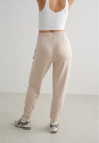 Beige Sweatpants verfügen über einen elastischen Bund, Seitentaschen und bündchen an den Knöcheln. Das Outfit wird mit silbernen und schwarzen Sportschuhen kombiniert.