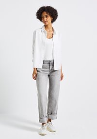 Camicia bianca a maniche lunghe sopra un top bianco, abbinata a jeans grigio chiaro con risvolti e sneakers bianche. Design e vestibilità semplici.