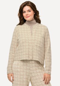 Beige gebreide cardigan met een rechte snit en open voorkant, voorzien van een subtiel patroon en lange mouwen. Draagt over een beige top.