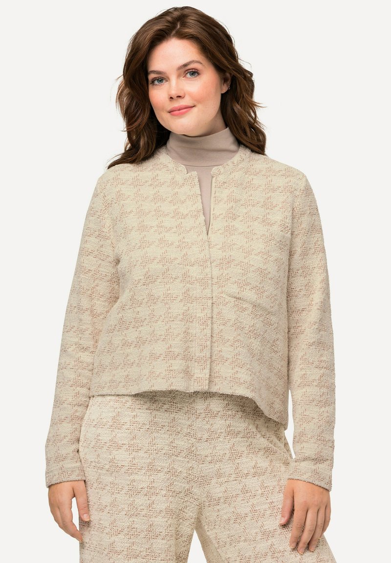 Beige gebreide cardigan met een rechte snit en open voorkant, voorzien van een subtiel patroon en lange mouwen. Draagt over een beige top.