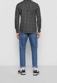 Camicia di flanella a quadri neri e grigi con polsini a bottone, abbinata a jeans azzurri arrotolati e sneakers nere con dettagli bianchi.