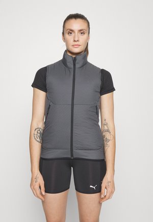 Γκρι γιλέκο με ψηλό γιακά και πλήρως φερμουάρ, που διαθέτει δύο πλαϊνές τσέπες. Φοριέται πάνω από ένα μαύρο κοντομάνικο μπλουζάκι και μαύρες σορτς.