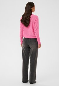 Un pull rose raccourci à manches longues et col rond, associé à un jean gris taille haute. Texture douce et design minimaliste.