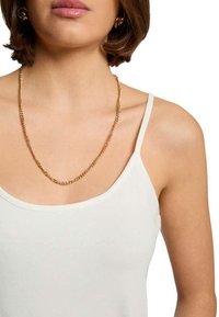 Collier en or avec des maillons entrelacés, porté par un modèle avec un débardeur blanc. Design simple, épaisseur moyenne et finition brillante.