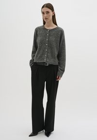 Cardigan grigio a maglia con bottoni anteriori, abbinato a pantaloni a gamba larga neri a vita alta e décolleté neri a punta. Tessuto morbido, vestibilità casual.