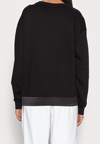 Svart sweatshirt med en texturerad, samlad nederkant, med rund hals och sänkt axeldesign. Tyget är mjukt och avslappnat.