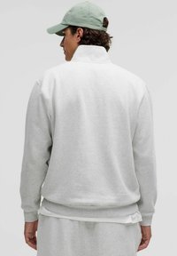 Hellgrauer Pullover mit hohem Kragen, gerippten Bündchen und Saum, aus weichem Material, über einem weißen Shirt getragen, von hinten betrachtet.