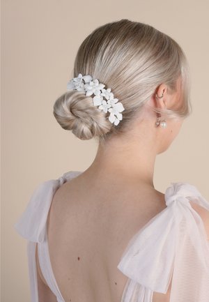 Clip per capelli floreale bianco decorato con piccole perle, fissato in un raccolto basso. I capelli sono biondi chiari, con una consistenza liscia e lucida.