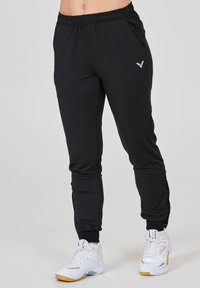 Sorte atletiske joggers med elastisk talje og sidelommer, prydet med et subtilt logo i grå. Stoffet ser glat og let ud.