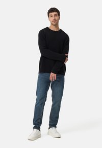 Svart ribbad tröja, blå jeans och vita sneakers. Tröjan har en lös passform med långa ärmar; jeansen har en rak bendesign.