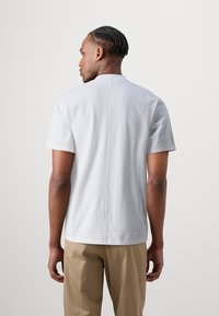 White cotton T-shirt with a crew neckline and short sleeves. Features a central seam on the back and a relaxed fit. Paired with beige trousers.