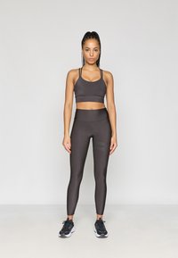 Tumehall spordibra õhukeste rihmadega ja sobivad kõrge puusaga retuusid, millel on sile tekstuur ja kerge triibuline detail. Mustad spordijalatsid.