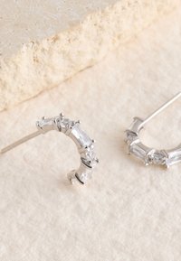 Silberne Creolen mit rechteckigen und runden klaren Edelsteinen, mit polierter Oberfläche und elegant geschwungenem Design.