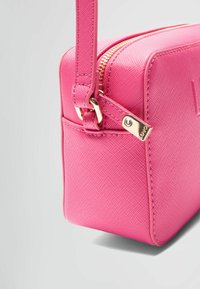 Růžová syntetická kabelka ve tvaru d clutch s texturovaným povrchem, zlatým zipem a krátkým popruhem na rameno. Kompaktní obdélníkový tvar.