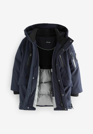 Veste isolée bleu marine avec une capuche amovible, dotée de multiples poches zippées, d'une doublure intérieure matelassée et d'une texture extérieure lisse.