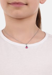 Collana in argento con un pendente a forma di coccinella con dettagli rosa e neri, indossata sopra una camicia bianca.