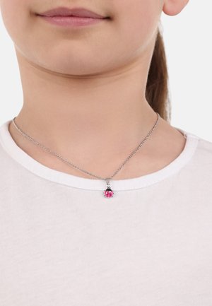 Silberne Halskette mit einem Marienkäfer-Anhänger in Pink und Schwarz, getragen über einem weißen Hemd.