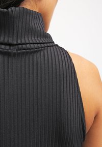 Svart ärmlös topp med hög krage, med vertikal ribbad struktur och slät yta. Visar en figursydd design och mjukt material.