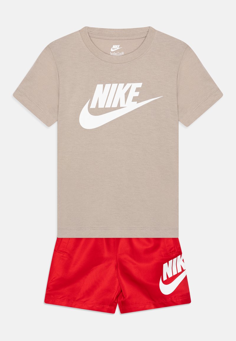 Beige pamut póló nagy fehér "Nike" logóval, piros selyem sorttal párosítva, amelynek oldalán szintén fehér "Nike" logó található.