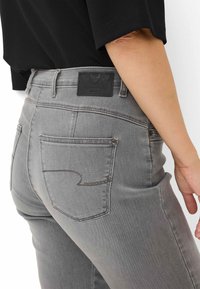 Jeans in denim grigio dal taglio aderente, con tasche posteriori e cuciture a contrasto. Un'etichetta in pelle nera del marchio è visibile in vita.