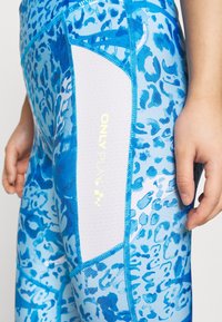 Siniset urheiluleggingsit, joissa on leopardi-kuvio, sisältävät vaaleansinisen verkkopaneelin ja neonkeltaisen "ONLY PLAY" -logon. Sileä rakenne.