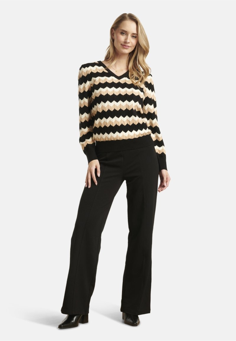 Black and cream zigzag patterned sweater with a V-neckline, paired with black flared pants and pointed black heels. Long sleeves and ribbed cuffs.