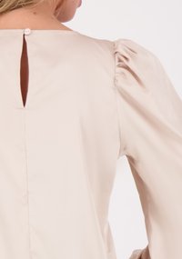 Lichtbeige blouse met pofmouwen, een gladde textuur, een keyhole-opening aan de achterkant en een enkele knoopsluiting.