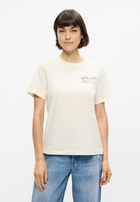 Κρέμα βαμβακ ερό t-shirt με στρογγυλή λαιμόκοψη, κοντά μανίκια και μικρή εκτυπωμένη γραφική παράσταση στο αριστερό στήθος. Χαλαρή εφαρμογή και μίνιμαλ σχεδίαση.