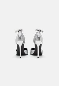 Zilveren high heels met een textuur bovenkant, verstelbare enkelband en een glanzende metalen hak met een zwarte zool.