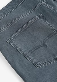 Jean en denim gris foncé avec une poche arrière unique, des détails de couture et une texture subtile.
