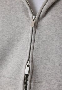Szara bluza z kapturem na suwak, wykonana z miękkiego materiału o gładkiej teksturze. Posiada metalowy zamek błyskawiczny oraz gładką białą podszewkę.